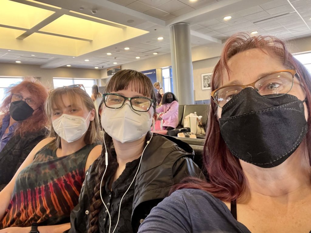 A woman, two teenage girls, and a long-haired guy wearing medical-type face masks in an airport.